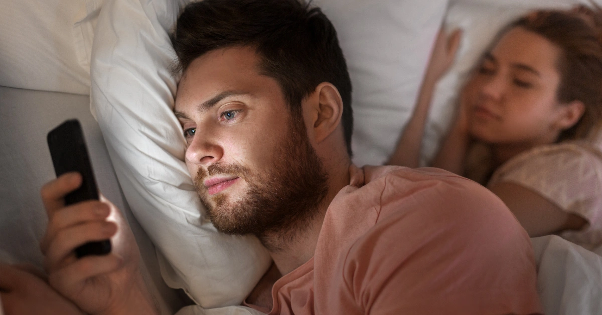 A guy on his cell phone while his partner is sleeping next to him