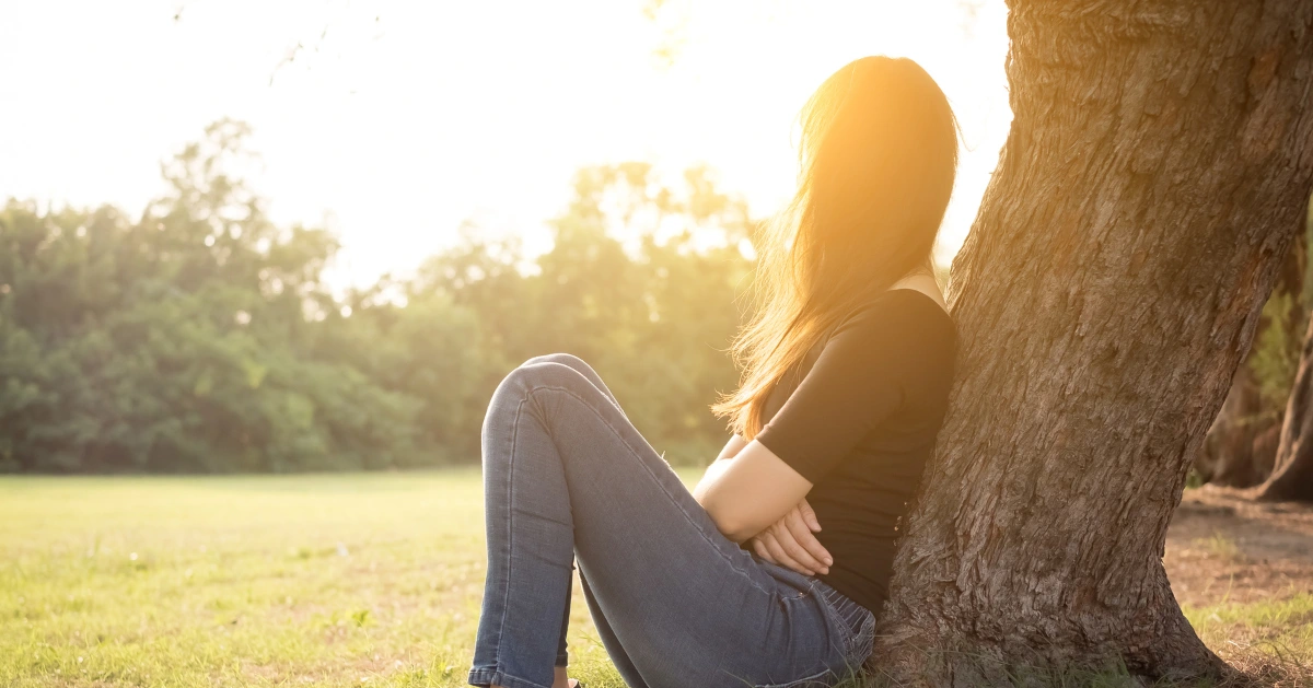 A girl sitting by a tree looking up to the sky