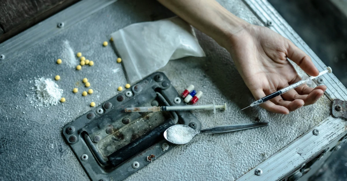 drugs on a chest box with someone's hand holding a needle