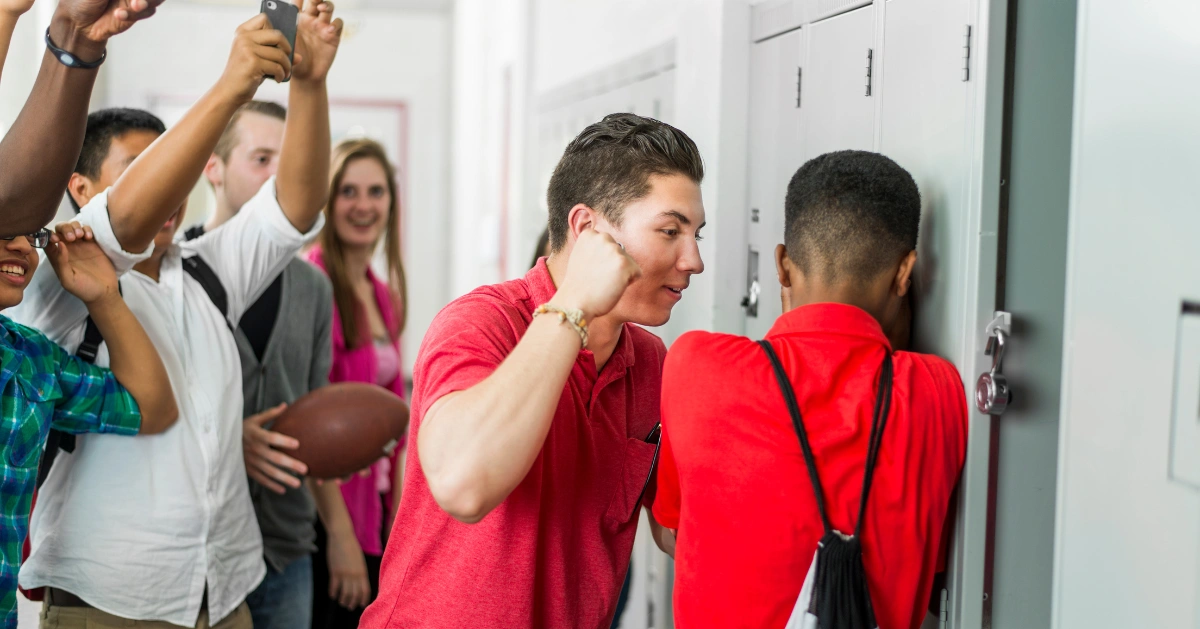 A teen boy bullying another teen boy while teens are standing around filming with their cell phones