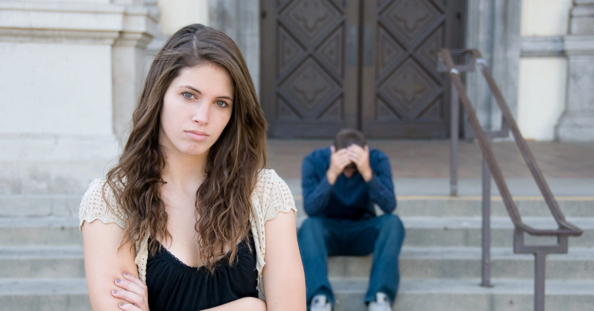 A girl looking at the camera while her ex boyfriend is sitting down