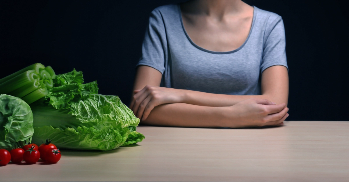 A girl sitting down with vegetables in front of her