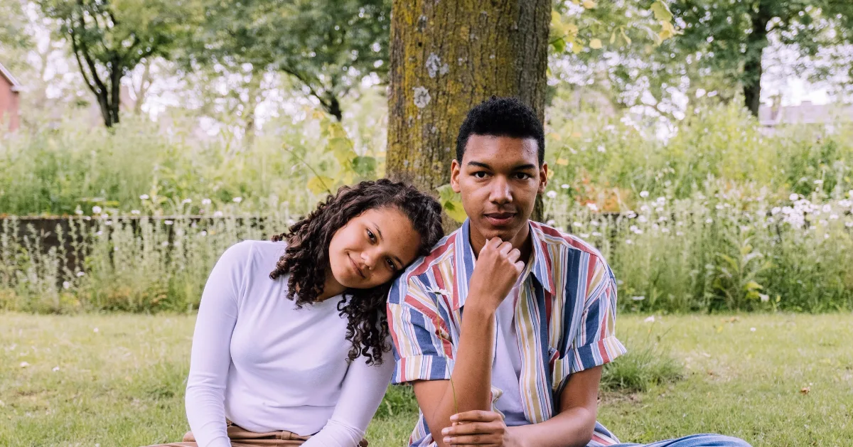 Guy and a girl sitting by a tree.