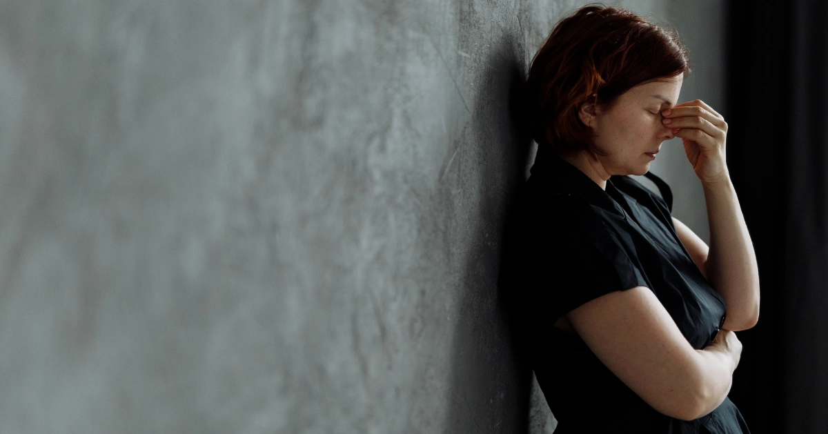 Lady leaning against a wall with her hand over her eyes