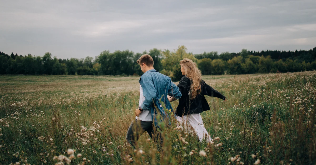 Couple running hand in hand in a field.