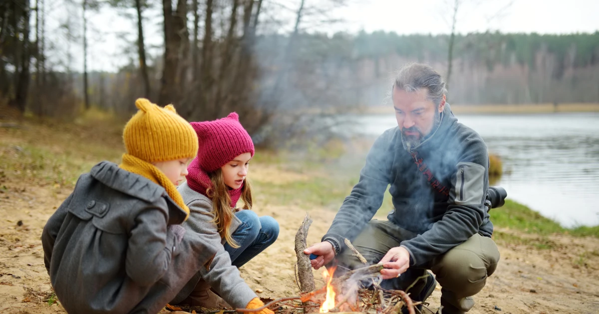 A dad with his two daughters sitting near a camp fire