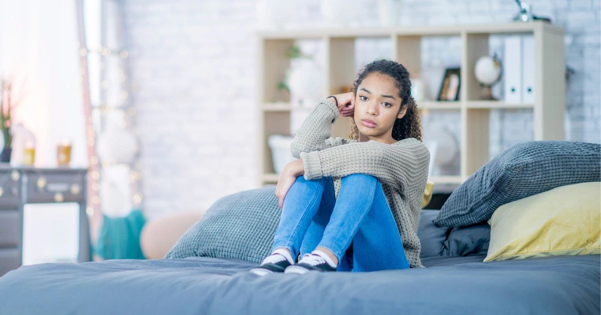 young teen girl sitting on her bed in deep thought