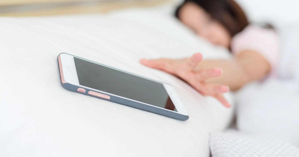 a lady lying in bed reaching for her cell phone