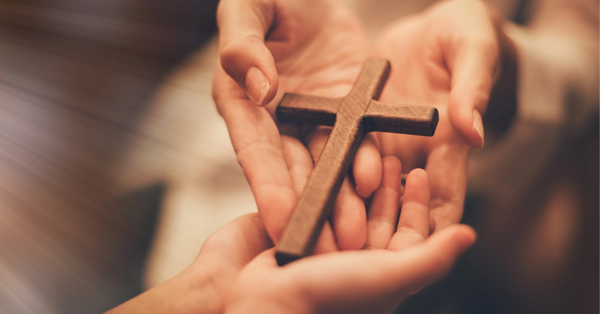 two pair of hands passing a wooden cross to each other
