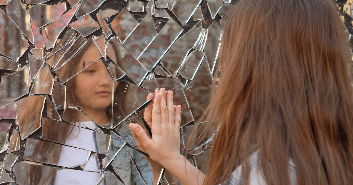 a young girl with her hand on a broken mirror
