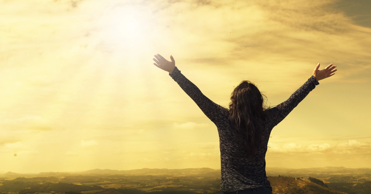 a girl with her arms up in the air looking up to the sky