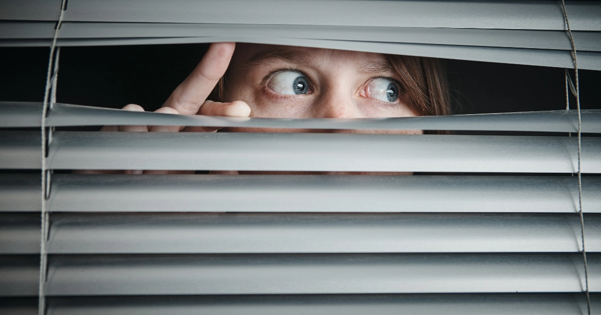 a person panicking looking through the blind of a window