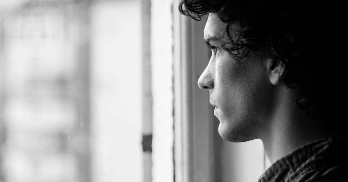 A guy looking out his window looking sad