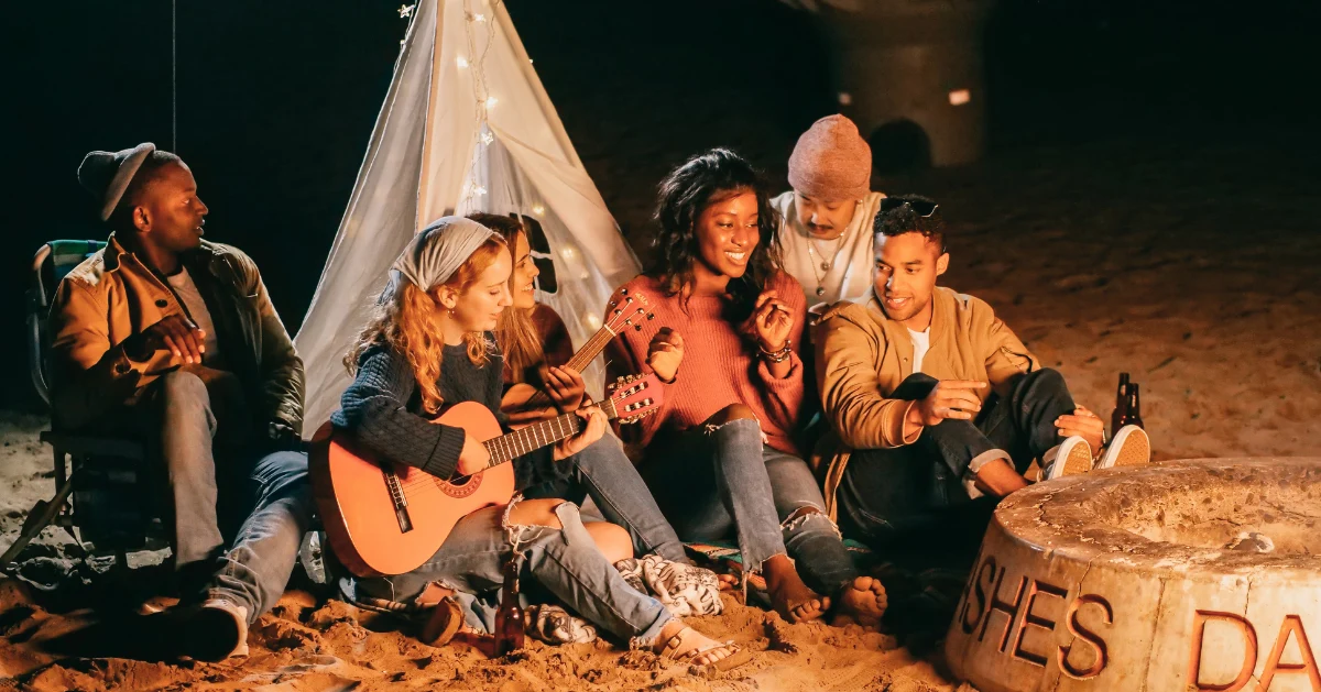Friends hanging out by a tent playing guitar.