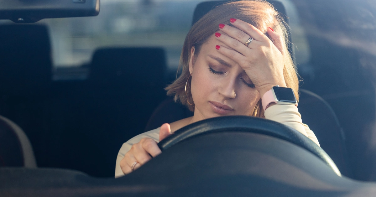 A woman sitting in her car looking sad.