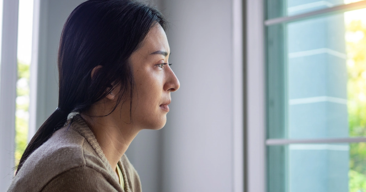A woman with a painful expression on her face looking out of her window.
