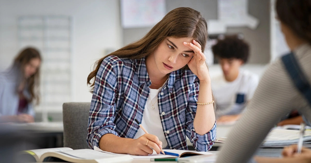 a young girl sitting at her desk in school with school pressure weighing on her