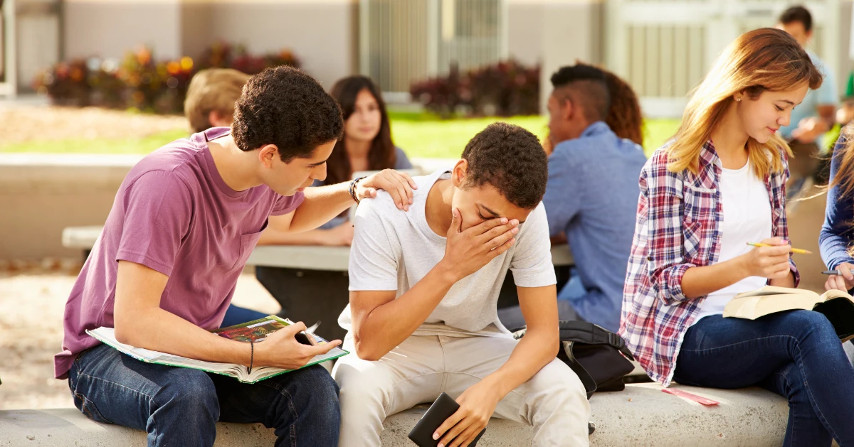 A teen boy upset while being comforted by his friend