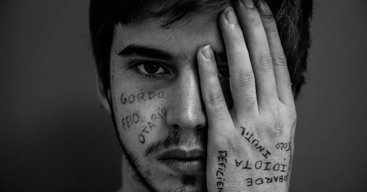 a guy with his hand coving one eye with bullying words written on his hand