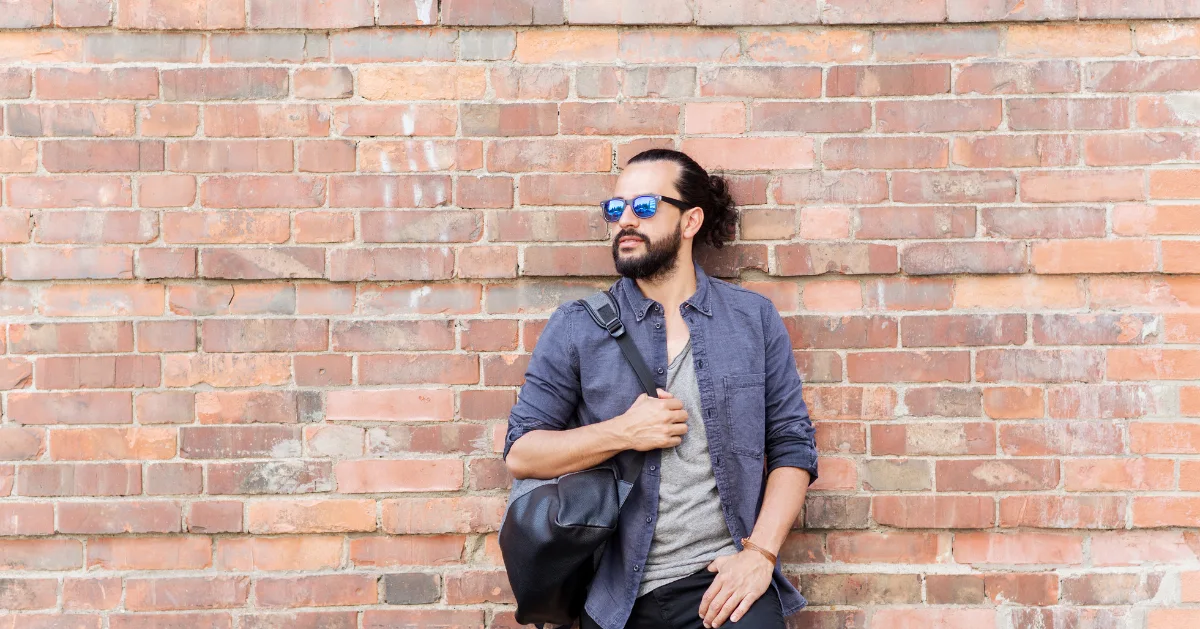 a guy leaning back on a brick wall while holding his bag