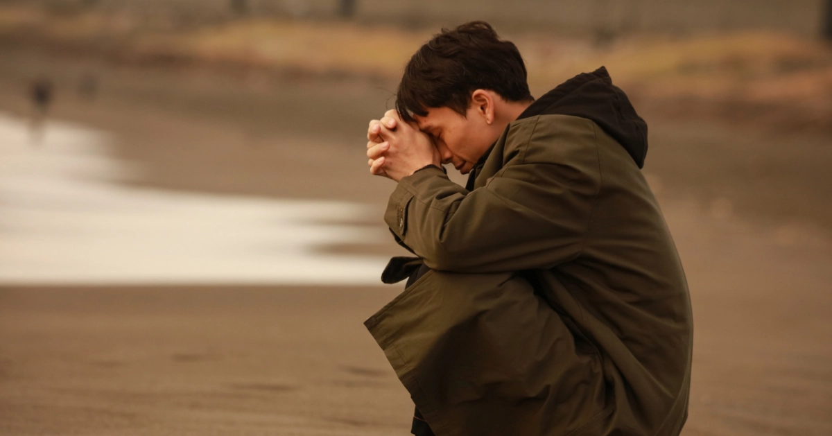 a guy sitting alone at the beach with his head down