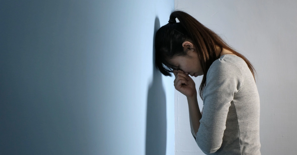 a girl standing at a wall with her head leading against it