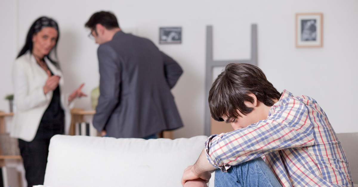 male teen sitting on coach while parents are fighting in background