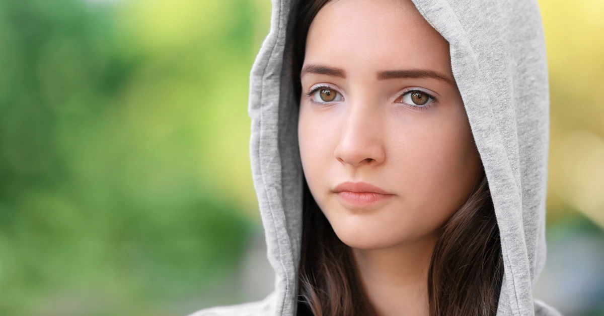 a young girl with a hoodie over her head. Her face shows pain