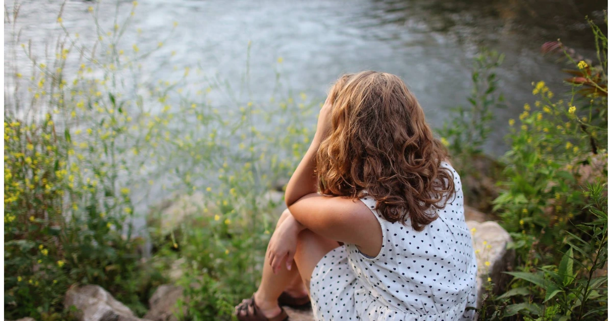 Girl with red hair sitting by a lake