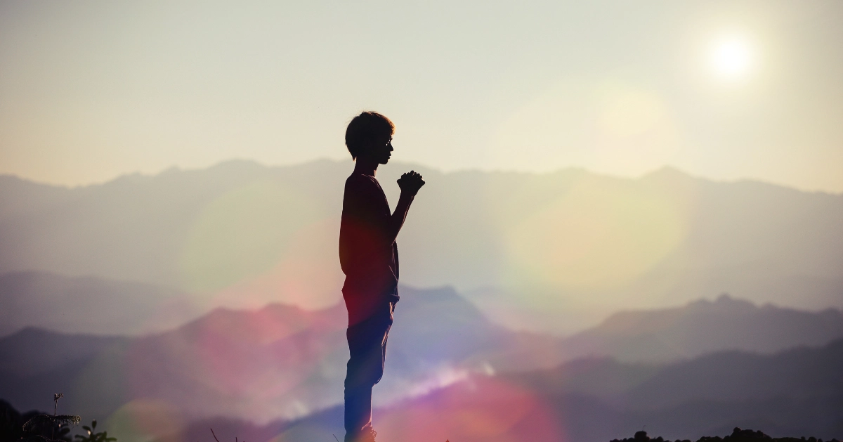 Silhouette of a Young man outside praying by mountains
